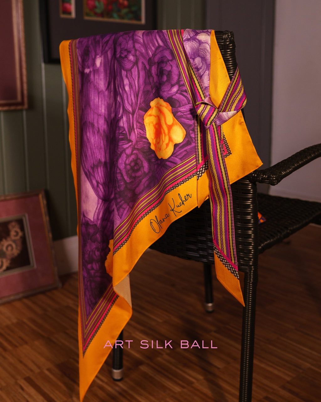 Large triangle silk scarf with floral print draped over a chair, styled with a matching Twilly ribbon tied in a bow.